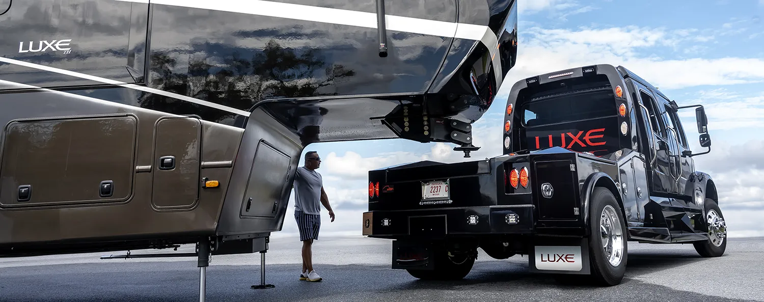 A luxury fifth wheel toy hauler, built by Luxe Fifth Wheel, with a Luxe Freightliner M2 106 in position to haul.